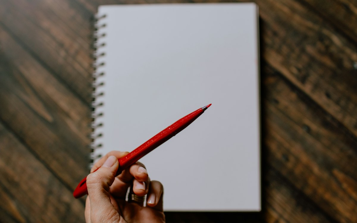 Hand holding a red pen over a blank notepad