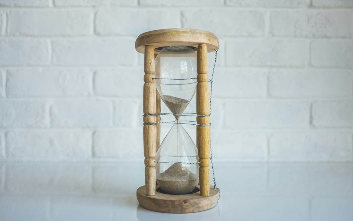 Wooden hourglass on a white table against a brick wall