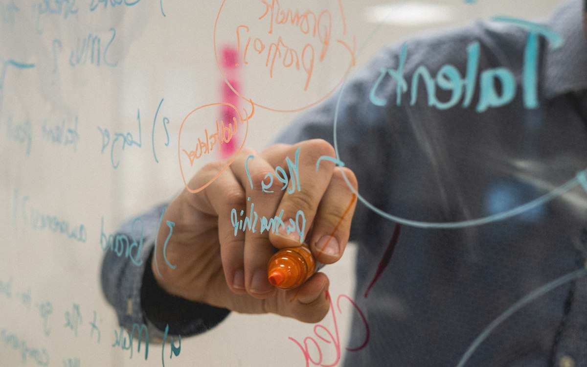 Person drawing a diagram on a glass whiteboard