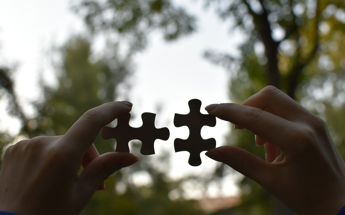 Two hands joining two puzzle pieces against the sky