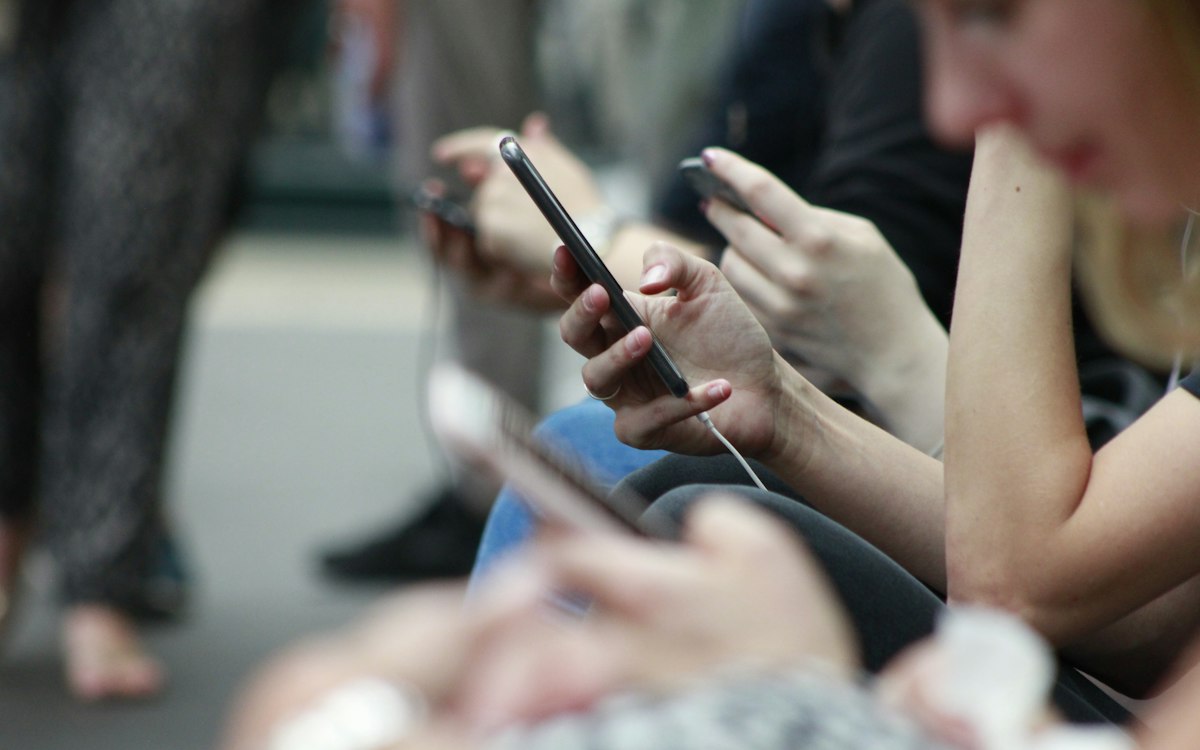 Yan yana oturup akıllı telefonlarında gezinen insanlar